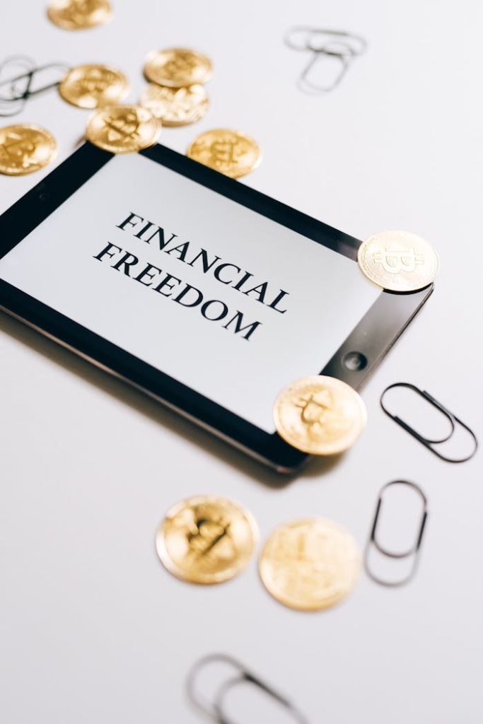 Coins are scattered around a digital tablet displaying Financial Freedom, symbolizing cryptocurrency wealth.